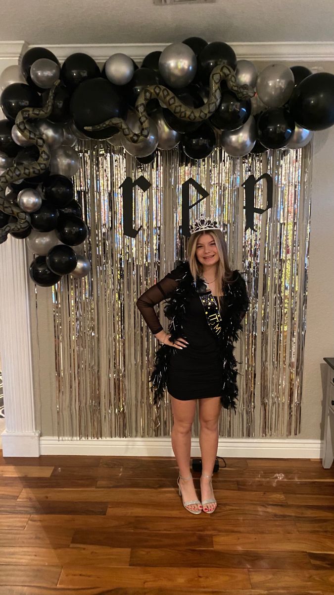 a woman standing in front of a balloon arch with black and silver balloons hanging from it