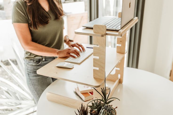 a woman using a laptop computer on a wooden stand next to a potted plant