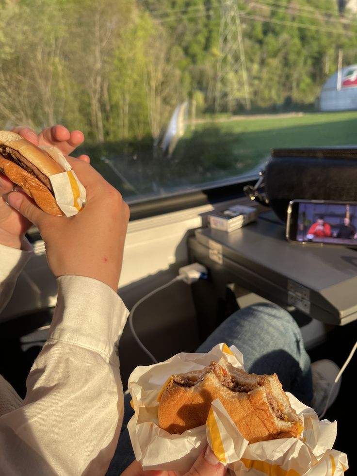 two people sitting in the back seat of a car eating hotdogs and sandwiches