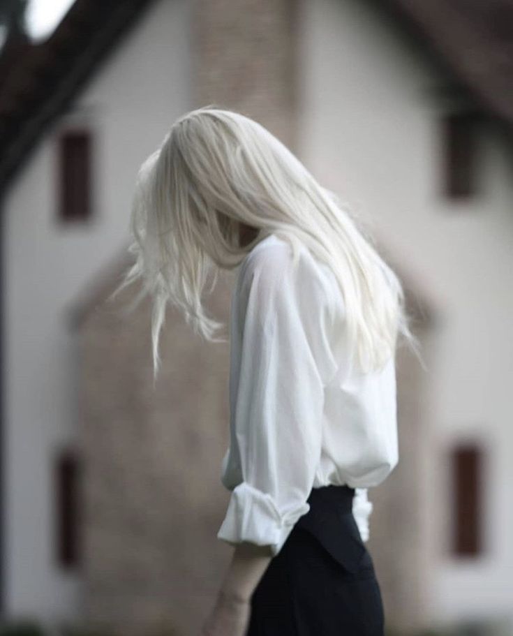 a woman with white hair is standing in front of a house wearing a black skirt