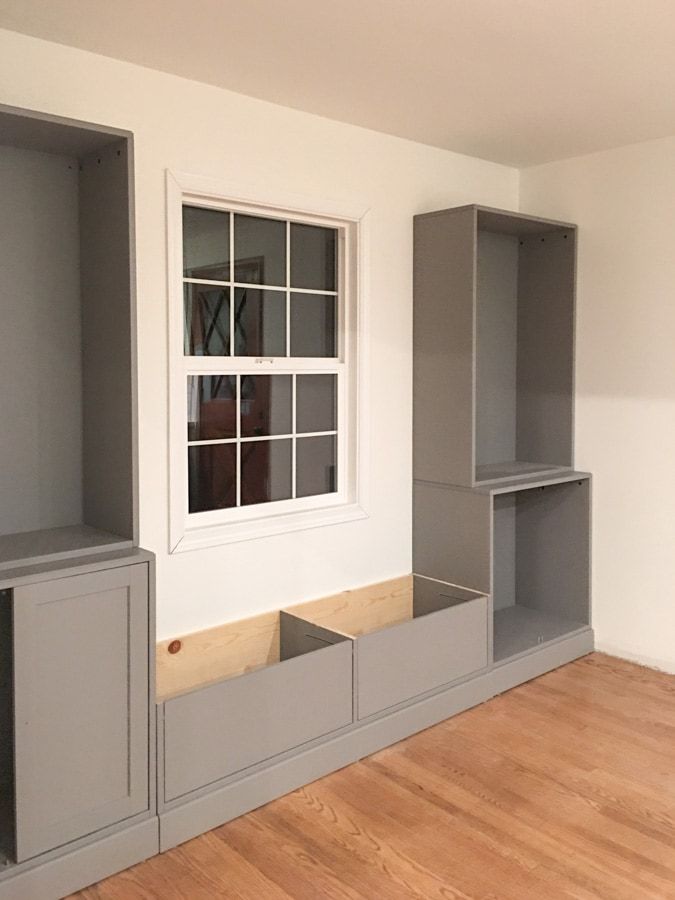 an empty room with gray cabinets and wood flooring in the foreground is a window