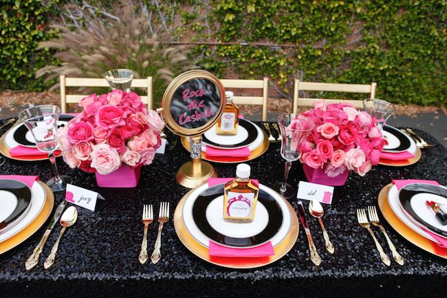 the table is set with black and gold plates, pink flowers, and napkins