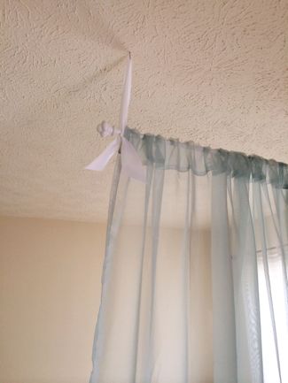 the curtains are hanging from the ceiling in front of the window with white ribbons on them