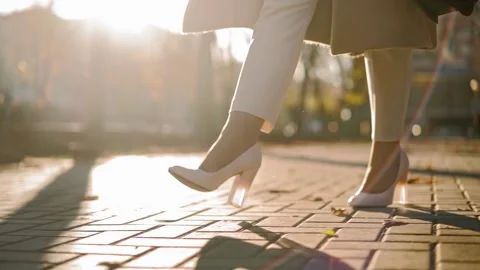 two women in white shoes walking down the street with their legs crossed and heels on