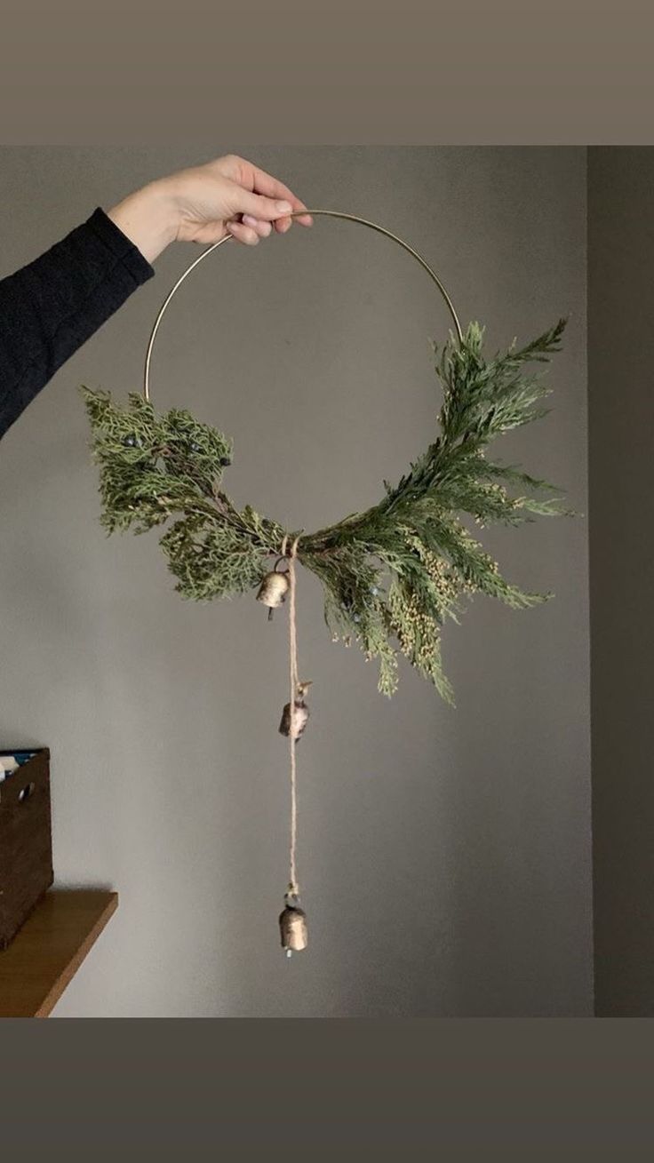 a person is holding a wreath with bells and pine cones on it, hanging from the ceiling