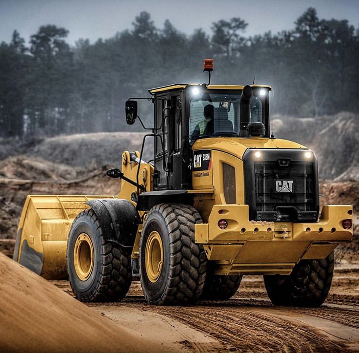 a yellow bulldozer is parked in the middle of a dirt field with trees in the background