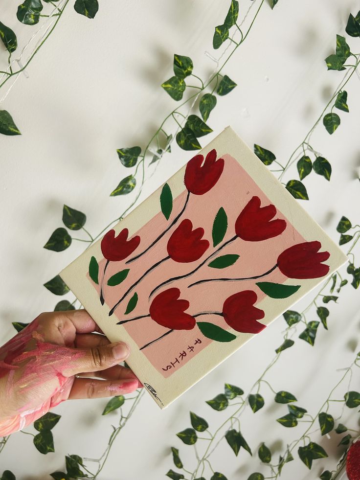 a hand holding up a card with red flowers on it and green leaves surrounding it