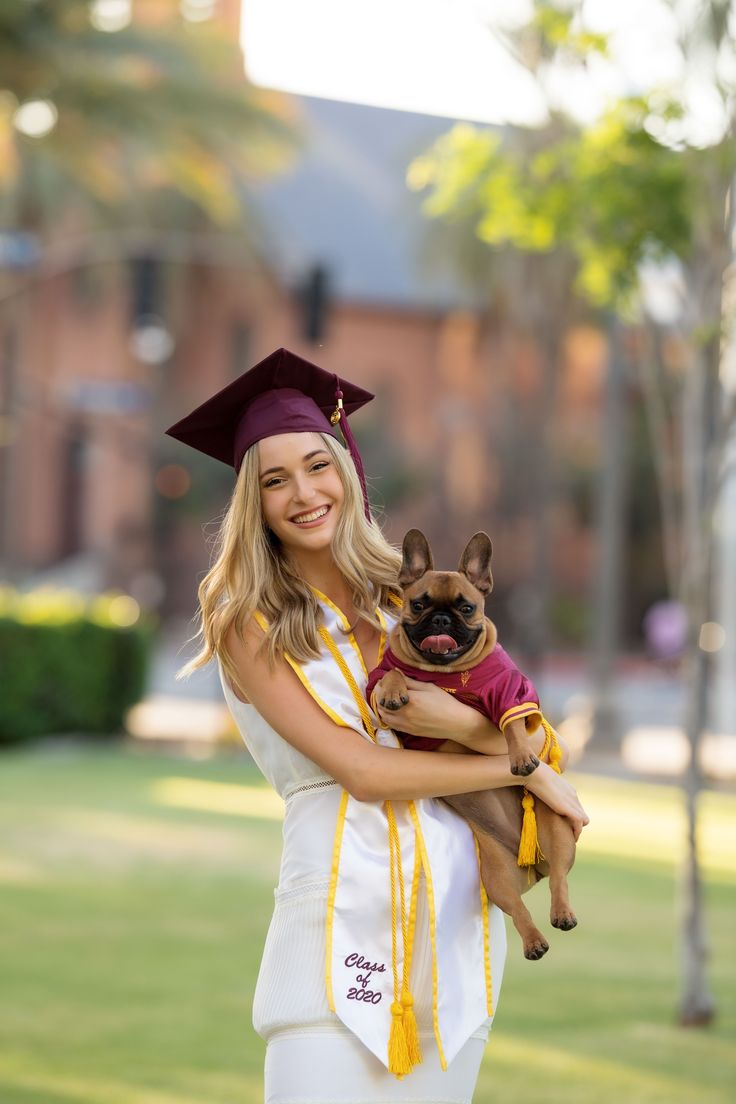 a woman holding a small dog in her arms and wearing a graduation cap on top of her head