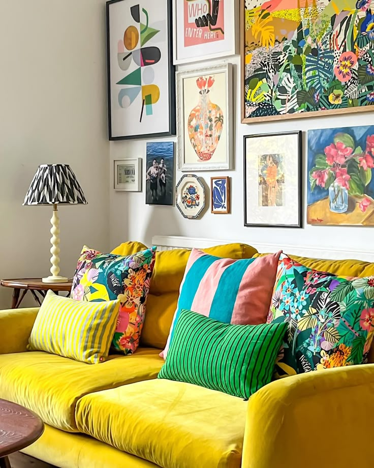 a living room filled with yellow couches covered in colorful pillows and pictures on the wall