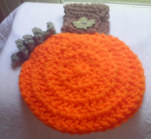 an orange crocheted hat sitting on top of a white bed next to a window