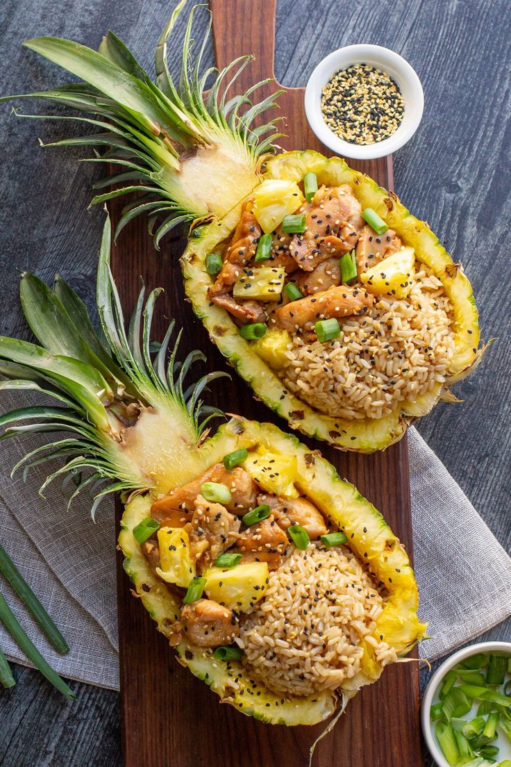 two pineapples on a cutting board topped with meat and vegtables