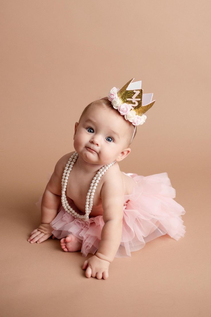 a baby girl wearing a pink tutu with a gold crown on her head and pearls around her neck