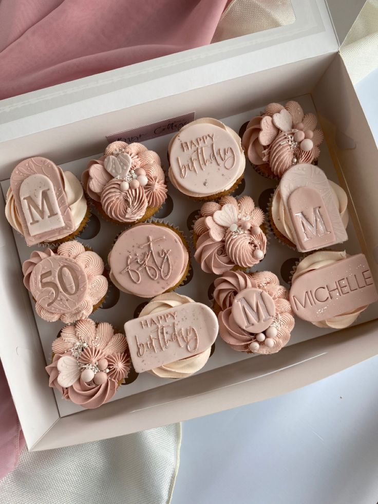 a box filled with cupcakes covered in frosting and decorated with pink icing