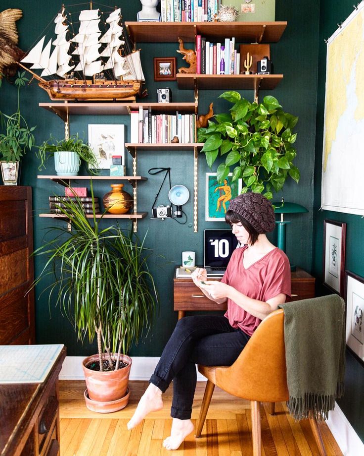 a woman sitting at a desk in front of a potted plant and bookshelf