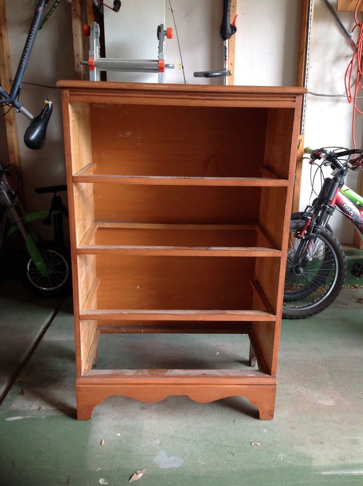 a wooden book shelf sitting in the middle of a room next to a bike and other bikes