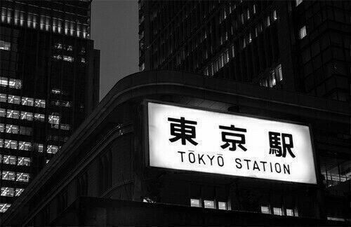 the tokyo station sign in black and white is lit up at night with skyscrapers behind it