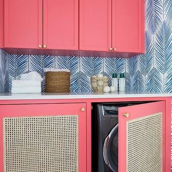 a washer and dryer in a room with pink cupboards, patterned wallpaper