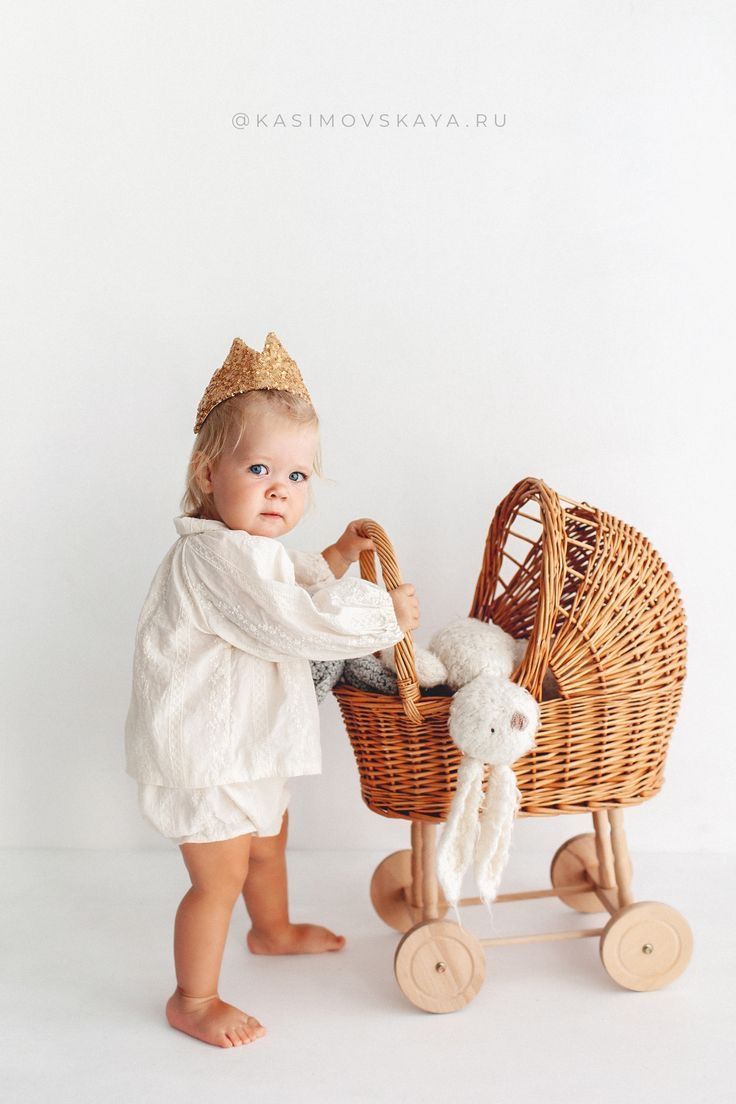 a small child in a white dress holding a teddy bear next to a wicker stroller