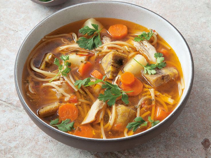 a bowl of chicken noodle soup with carrots and parsley on the side