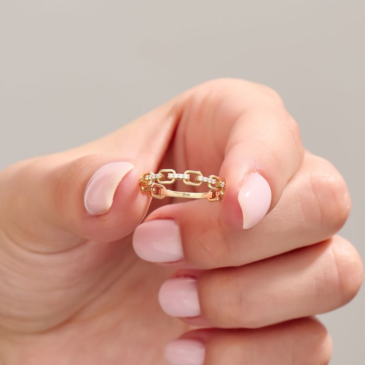 a woman's hand holding a gold ring that has two links on the middle