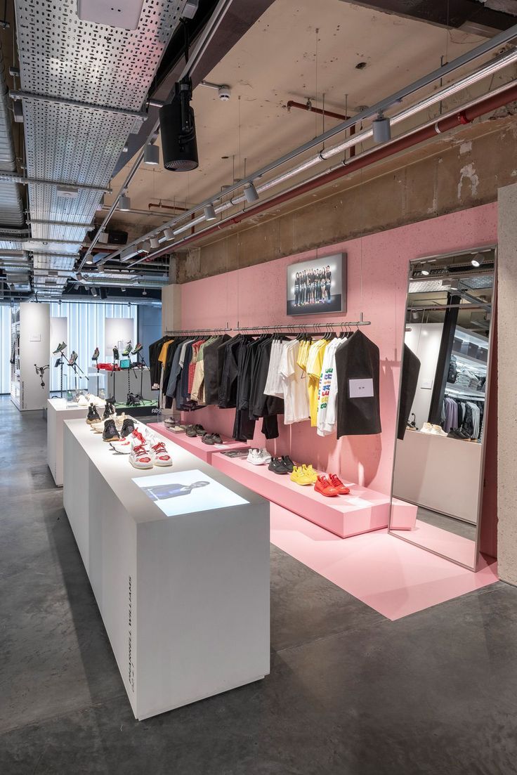 the inside of a clothing store with pink walls and white tables on either side of it