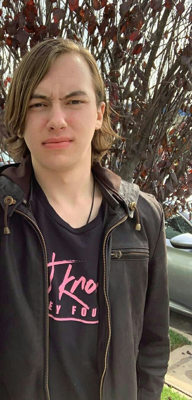 a young man standing in front of a tree with no leaves on his head and wearing a black jacket