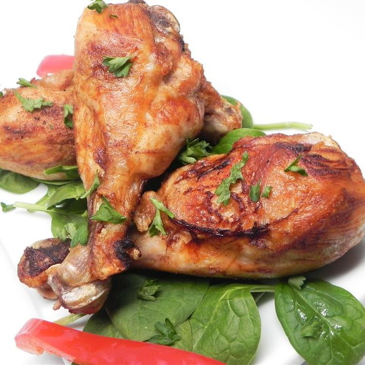 two pieces of chicken sitting on top of spinach leaves and red hot peppers next to them