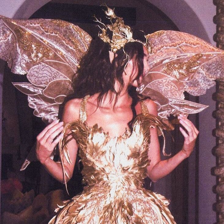 a woman in a gold dress with wings on her head and hands behind her back