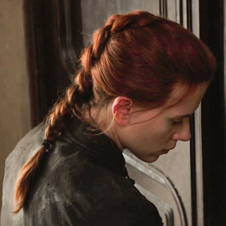 a woman with red hair wearing a black leather jacket and looking down at her cell phone