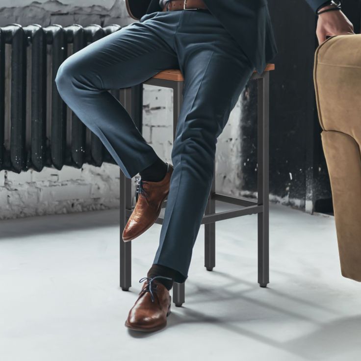 a man in a suit sitting on a chair with his legs crossed and wearing brown shoes