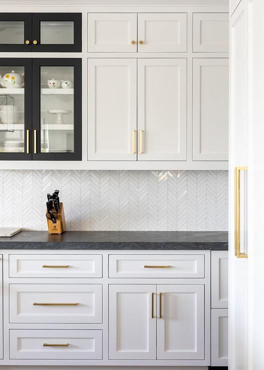 a kitchen with white cabinets and black counter tops, gold pulls on the cupboards