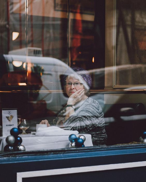 an older woman sitting at a table in front of a window