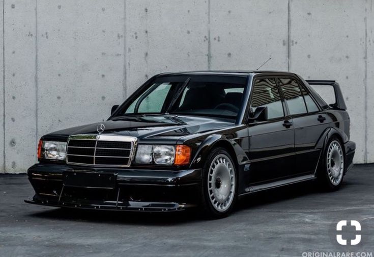 a black mercedes benz is parked in front of a white wall