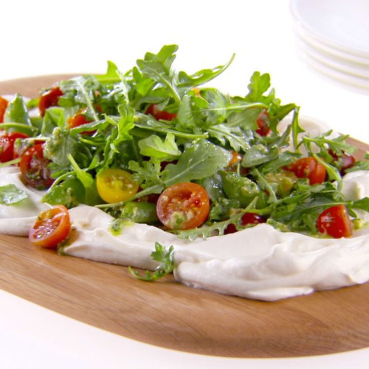 a salad with tomatoes, cheese and lettuce on a wooden platter next to plates