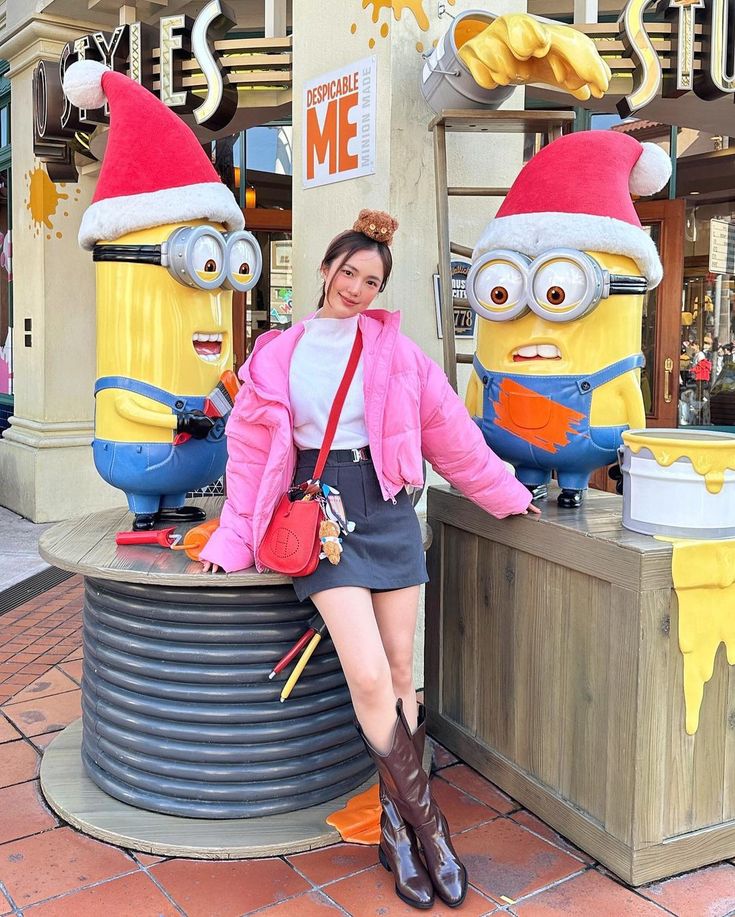 a woman posing in front of a statue of two minion characters wearing santa hats