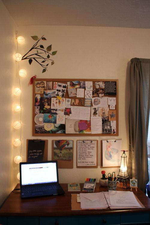 a laptop computer sitting on top of a wooden desk in front of a wall covered with pictures