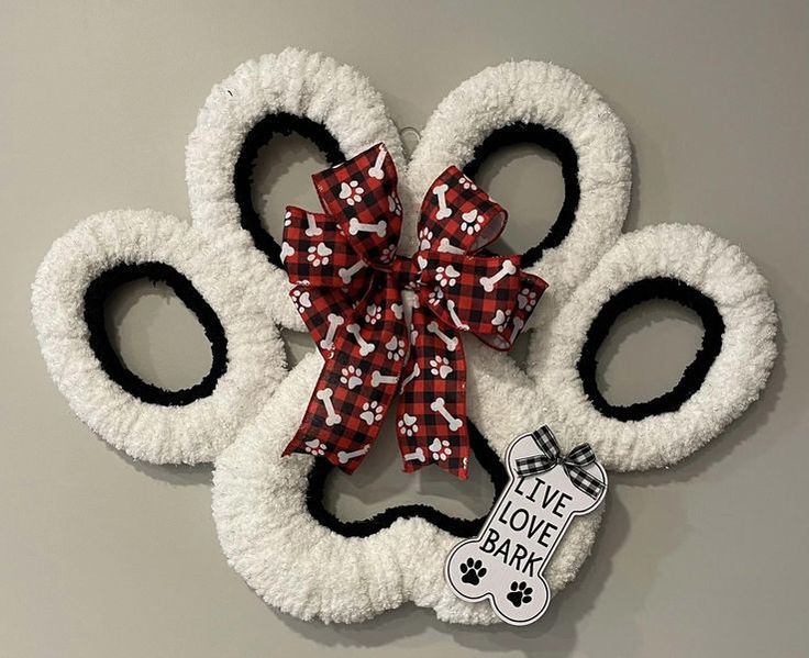 a white dog paw shaped wreath with a red and black bow on it's head