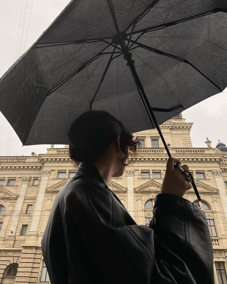 a woman holding an open umbrella in front of a large building on a cloudy day