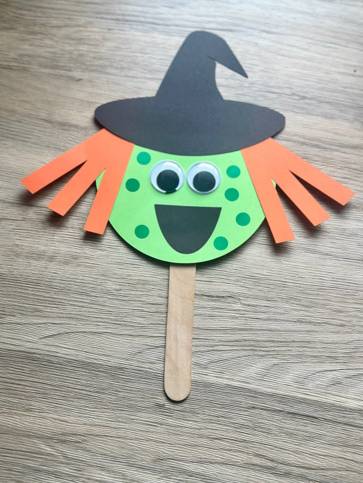 a green and orange paper witch on a wooden stick