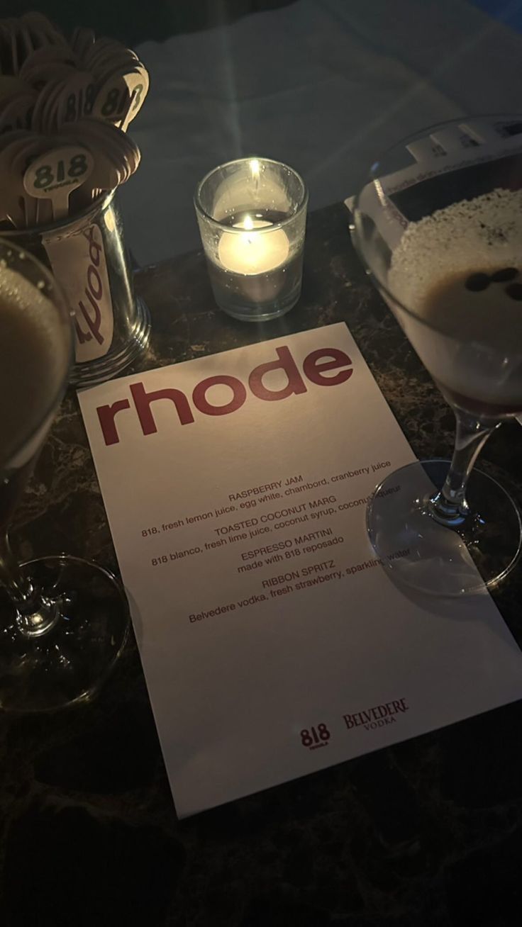 a table with two glasses and a menu sitting on top of it next to candles