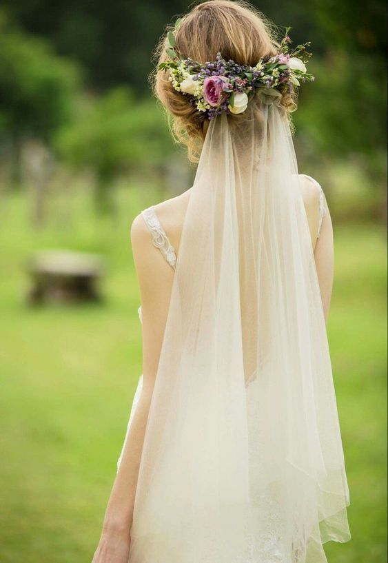 a woman wearing a veil and flowers in her hair is looking at the ground outside