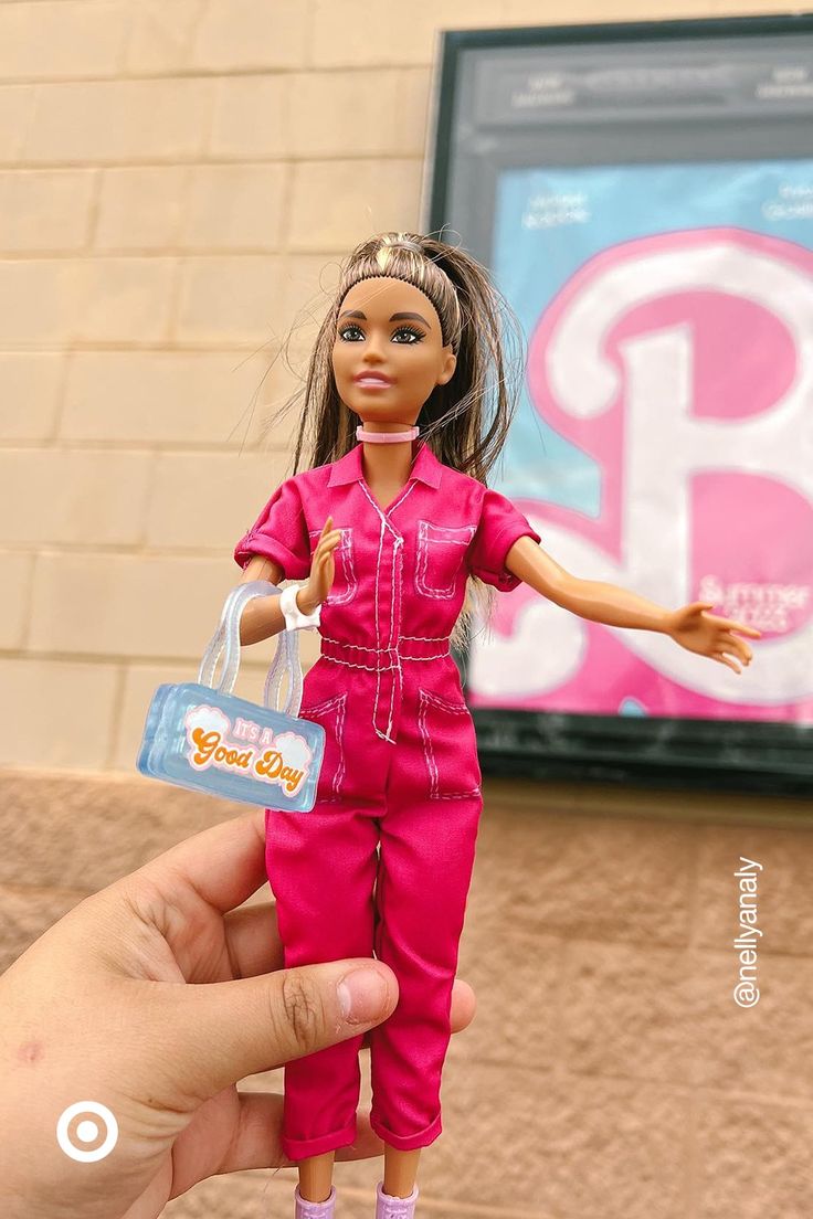 a hand is holding a barbie doll in front of a sign with the letter p on it