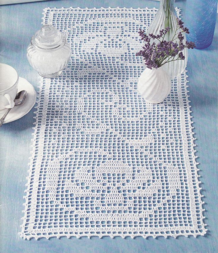 a crocheted doily with flowers in a vase on a blue table cloth