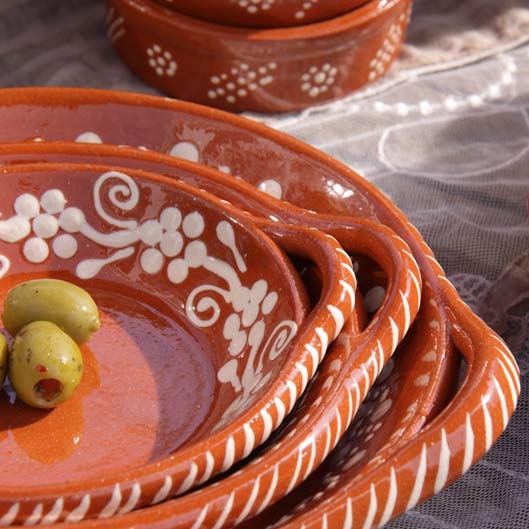 an orange bowl filled with olives on top of a white table cloth next to other bowls