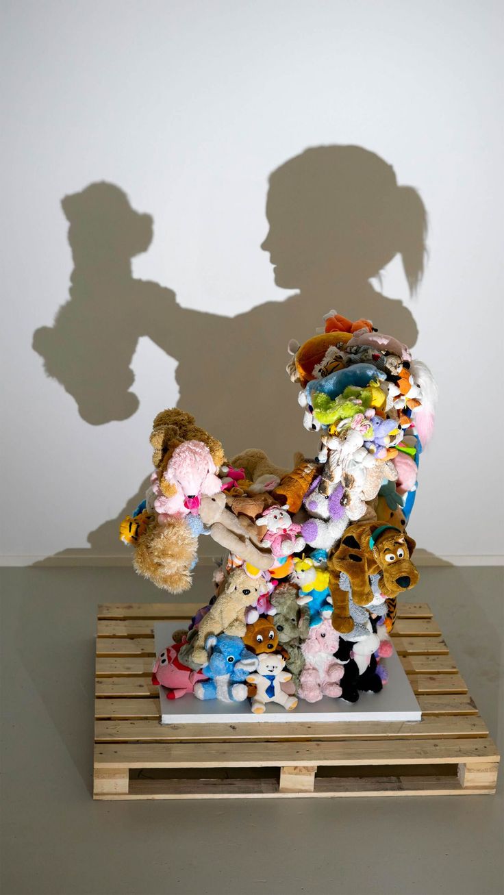 the shadow of a person holding a teddy bear in front of a pile of stuffed animals