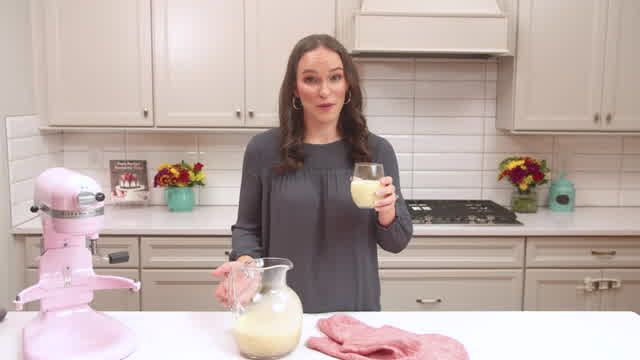 a woman standing in a kitchen with a blender and mixer on the counter next to her