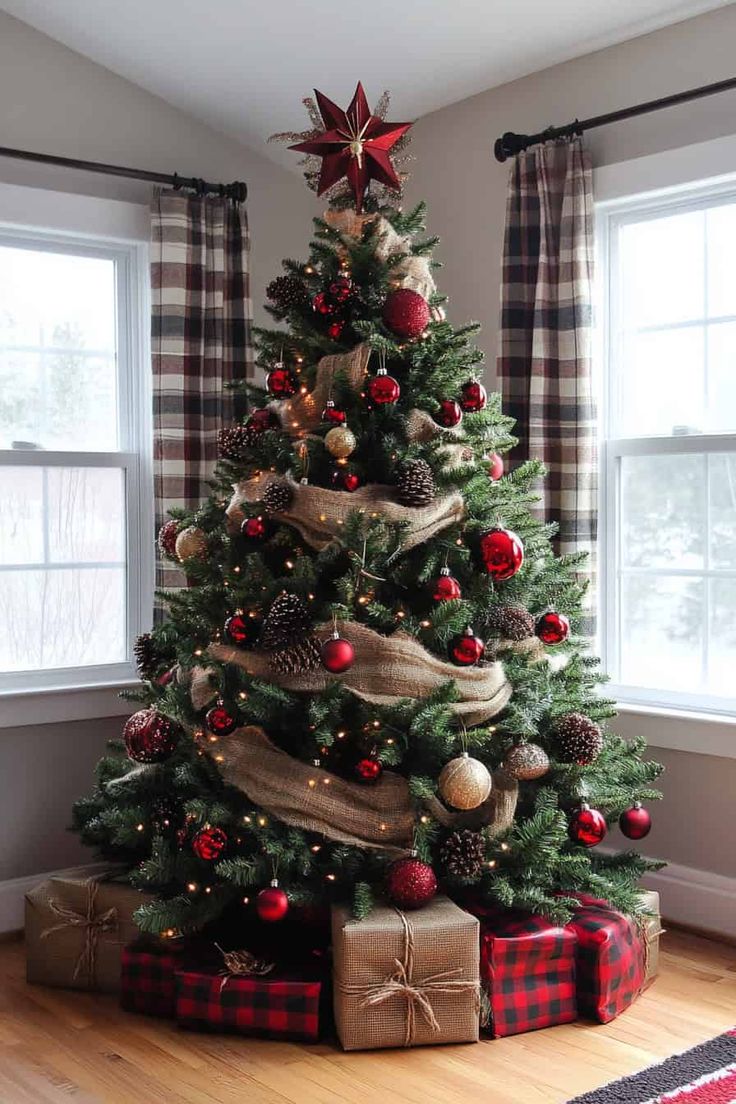 a christmas tree with presents under it in a living room next to two large windows