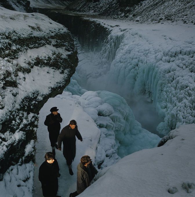 several people are walking along the side of a frozen waterfall