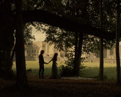 a man and woman holding hands in front of a castle with trees on both sides