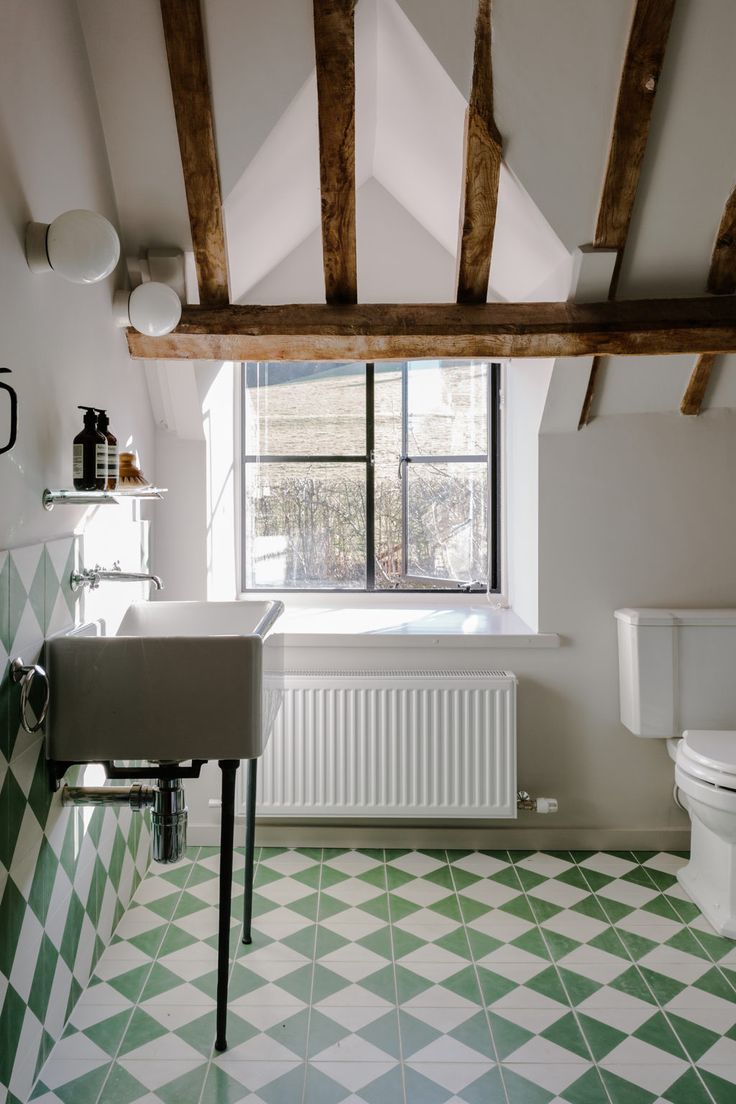 a bathroom with green and white checkered flooring next to a toilet, sink and window